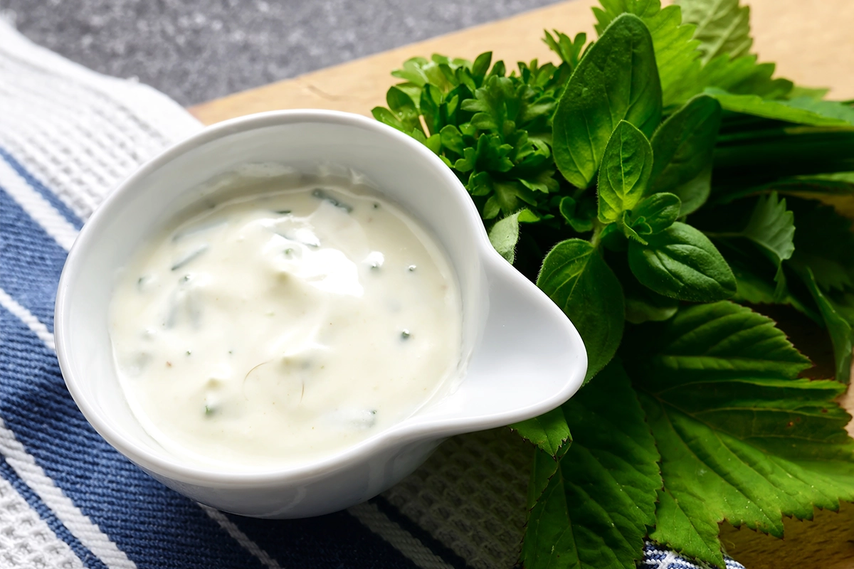 Image showing a bowl of freshly made 4 ingredient tartar sauce beside ingredients of mayonnaise, chopped pickles, fresh dill, and mustard, ready to accompany a seafood dish.