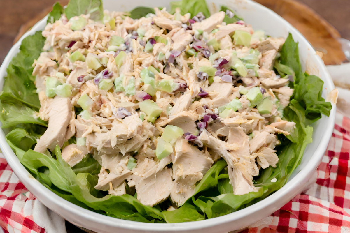 A bowl of freshly prepared chicken salad without celery, featuring alternative crunchy ingredients like sliced almonds and chopped apples, served on a bright kitchen table.