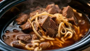 Crock pot filled with savory beef and noodles, steam rising